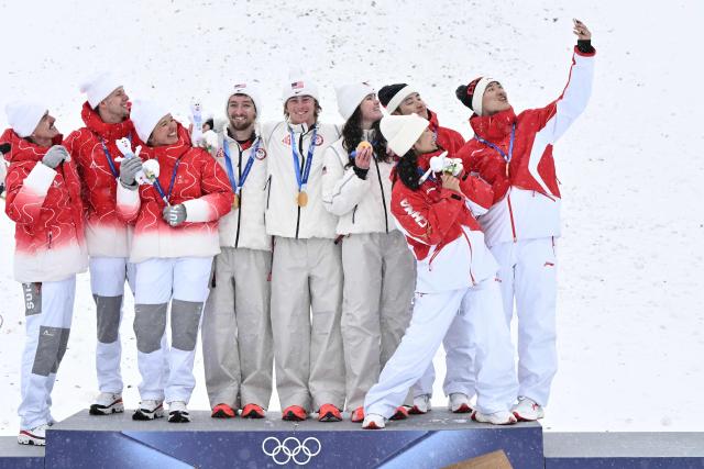 (From L) Silver medallists Switzerland's Noe Roth, Switzerland's Pirmin Werner and Switzerland's Lina Kozomara, gold medallists USA's Christopher Lillis, USA's Connor Curran and USA's Kaila Kuhn, and bronze medallists China's Xu Mengtao, China's Li Tianma, and China's Wang Xindi celebrate on the podium after the freestyle skiing mixed team aerials final during the Milano Cortina 2026 Winter Olympic Games at Livigno Aerials & Moguls Park, in Livigno (Valtellina), on February 21, 2026. (Photo by Jeff PACHOUD / AFP)