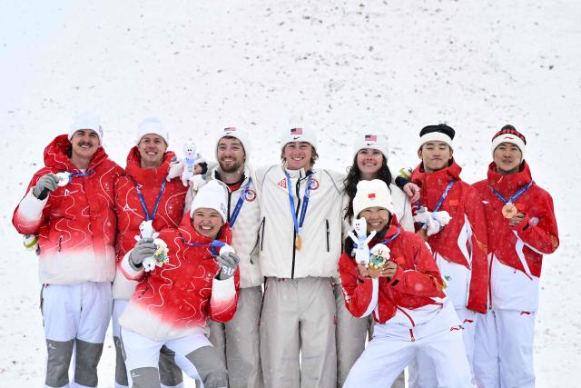 (From L) Silver medallists Switzerland's Noe Roth, Switzerland's Pirmin Werner and Switzerland's Lina Kozomara, gold medallists USA's Christopher Lillis, USA's Connor Curran and USA's Kaila Kuhn, and bronze medallists China's Xu Mengtao, China's Li Tianma, and China's Wang Xindi celebrate on the podium after the freestyle skiing mixed team aerials final during the Milano Cortina 2026 Winter Olympic Games at Livigno Aerials & Moguls Park, in Livigno (Valtellina), on February 21, 2026. (Photo by Jeff PACHOUD / AFP)