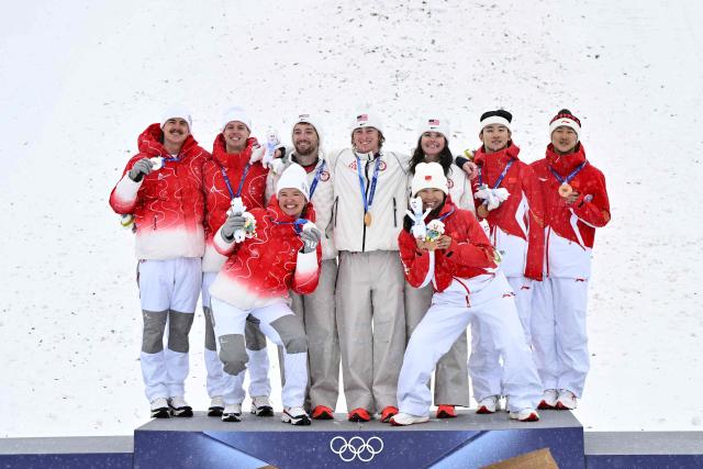 (From L) Silver medallists Switzerland's Noe Roth, Switzerland's Pirmin Werner and Switzerland's Lina Kozomara, gold medallists USA's Christopher Lillis, USA's Connor Curran and USA's Kaila Kuhn, and bronze medallists China's Xu Mengtao, China's Li Tianma, and China's Wang Xindi celebrate on the podium after the freestyle skiing mixed team aerials final during the Milano Cortina 2026 Winter Olympic Games at Livigno Aerials & Moguls Park, in Livigno (Valtellina), on February 21, 2026. (Photo by Jeff PACHOUD / AFP)