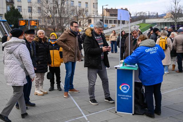 Hungarian MP Zsolt Greczy (C) of the Democratic Coalition (DK) checks his phone while collecting voters' signatures in central Budapest on February 21, 2026, as the campaign season officially begins in Hungary. Less than two months before the general election, candidates must collect signatures from at least 500 people in their district to run in the April 12, 2026 vote. (Photo by Attila KISBENEDEK / AFP)