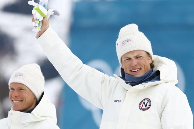 Silver medallist Norway's Martin Loewstroem Nyenget (L) and gold medallist Norway's Johannes Hoesflot Klaebo celebrate during a podium ceremony for the men's cross country 50km mass start final event of the Milano Cortina 2026 Winter Olympic Games at Tesero Cross-Country Skiing Stadium in Lago di Tesero (Val di Fiemme) on February 21, 2026. (Photo by Anne-Christine POUJOULAT / AFP)