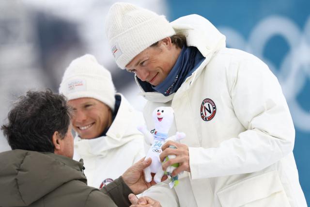 Silver medallist Norway's Martin Loewstroem Nyenget (L) and gold medallist Norway's Johannes Hoesflot Klaebo celebrate during a podium ceremony for the men's cross country 50km mass start final event of the Milano Cortina 2026 Winter Olympic Games at Tesero Cross-Country Skiing Stadium in Lago di Tesero (Val di Fiemme) on February 21, 2026. (Photo by Anne-Christine POUJOULAT / AFP)
