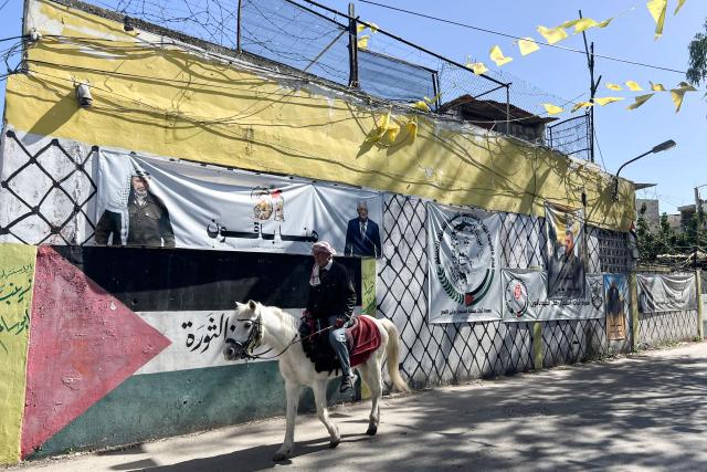 A Palestinian man rides an Arabian horse past a banner depicting the Palestinian leader Yasser Arafat (L) and the current leader Mahmud Abbas, the day after an Israeli strike on the Palestinian refugee camp in Ain al-Hilweh, near the coastal city of Sidon, in southern Lebanon on February 21, 2026. Lebanon's health ministry said 10 people were killed on February 20, 2026, in the east and two in the south of the country both areas where Hezbollah holds sway. The strikes come as tensions are brewing between the United States and Iran, with the US president threatening military action over the Islamic republic's nuclear programme. (Photo by Mahmoud ZAYYAT / AFP)