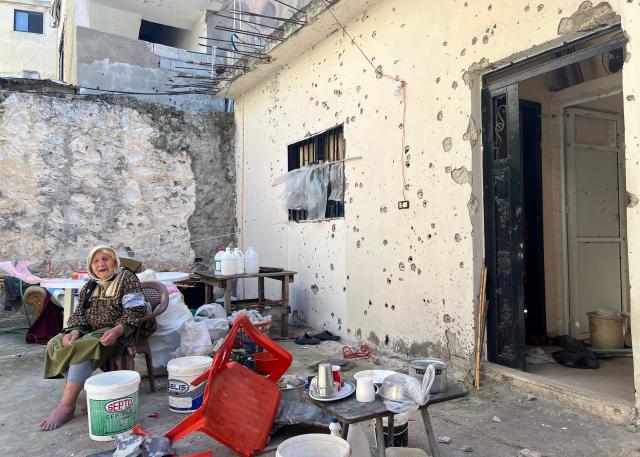 A Palestinian woman sits in the yard outside her home opposit a destroyed building the day after an  Israeli strike on the Palestinian refugee camp in Ain al-Hilweh, near the coastal city of Sidon, in southern Lebanon on February 21, 2026. Lebanon's health ministry said 10 people were killed on February 20, 2026, in the east and two in the south of the country both areas where Hezbollah holds sway. The strikes come as tensions are brewing between the United States and Iran, with the US president threatening military action over the Islamic republic's nuclear programme. (Photo by Mahmoud ZAYYAT / AFP)