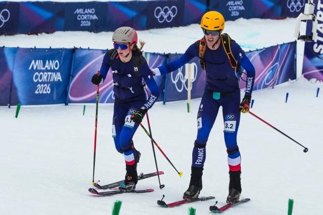 France's Thibault Anselmet (R) hands over to France's Emily Harrop as they compete in the mixed relay ski mountaineering race during the Milano Cortina 2026 Winter Olympic Games at the Stelvio Ski Centre in Bormio (Valtellina) on February 21, 2026. (Photo by Dimitar DILKOFF / AFP)