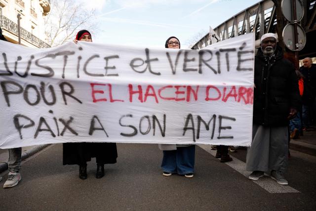 Protesters hold a banner during a march to demand justice for El Hacen Diarra, who died in January in police custody at a police station, in Paris on February 21, 2026. The 35-year-old Mauritanian man died during the night of January 15-16 while in police custody at the 20th arrondissement police station in Paris, after being arrested outside his workers' hostel. His family has denounced police violence, and a video shot by a neighbor shows two police officers, one of whom is kneeling and punching the man on the ground twice. (Photo by Charlotte SIEMON / AFP)