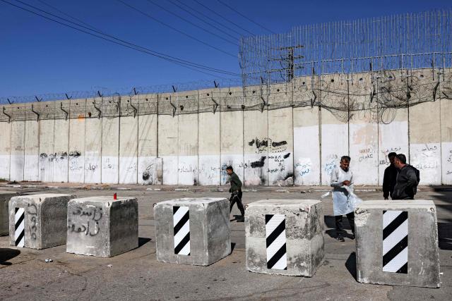 Men walk past concrete barrier blocks installed by Israeli police the prior week alongside Israel's controversial separation barrier in Israeli-annexed east Jerusalem across from Beit Hanina on February 21, 2026. (Photo by AHMAD GHARABLI / AFP)