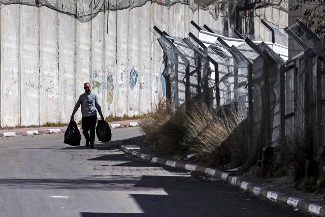 A man walks with sacks by Israel's controversial separation barrier in Israeli-annexed east Jerusalem across from Beit Hanina on February 21, 2026. (Photo by AHMAD GHARABLI / AFP)