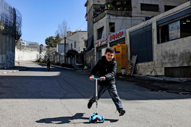 A boy rides a scooter near Israel's controversial separation barrier in Israeli-annexed east Jerusalem across from Beit Hanina on February 21, 2026. (Photo by AHMAD GHARABLI / AFP)