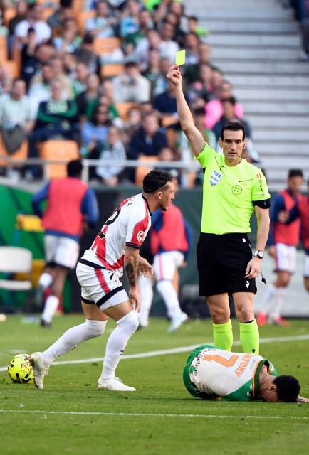 Spanish referee Juan Martinez Munuera presents a yellow card to Rayo Vallecano's Uruguayan defender #22 Alfonso Espino as Real Betis' Brazilian forward #07 Antony lies on the field during the Spanish league football match between Real Betis and Rayo Vallecano de Madrid at Benito Villamarin Stadium in Seville on February 21, 2026. (Photo by CRISTINA QUICLER / AFP)