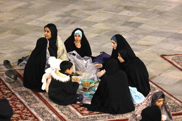 An Iranian family sits together to break the dawn to dusk Ramadan fast during Iftar, in the grounds of the Imamzadeh Saleh mosque in Tehran on February 21, 2026. Muslims throughout the world are marking the month of Ramadan, the holiest month in the Islamic calendar, during which devotees fast from dawn until dusk. (Photo by ATTA KENARE / AFP)