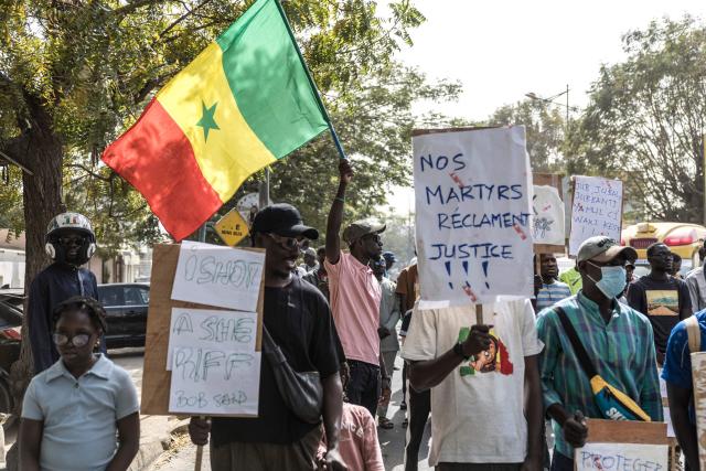 An activist waves a Senegalese flag during a demonstration demanding an end to police blunders and bring justice to the victims in Dakar on February 21, 2026. Students and pupils organizations, as well as activists, marched in Dakar on Saturday to “demand an end to police blunders and bring justice to the victims,” following the death of a student during a police operation at a university in the capital in early February. Abdoulaye Ba, a second-year medical student, died on February 9 on the campus of Cheikh Anta Diop University (UCAD) during a police operation, after several days of demonstrations and clashes between police and students protesting a reform of scholarship payments and demanding the settlement of arrears. (Photo by PATRICK MEINHARDT / AFP)