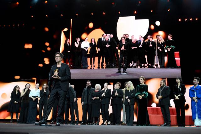 German film director ?lker Catak (C) holds the Golden Bear for Best Film he was given for his movie "Gelbe Briefe (Yellow Letters)" during the Award Ceremony of the 76th Berlinale, Europe's first major film festival of the year, in Berlin on February 21, 2026. The 76th Berlin Film Festival draws to a close after 10 days, with 22 films in competition. (Photo by RALF HIRSCHBERGER / AFP)