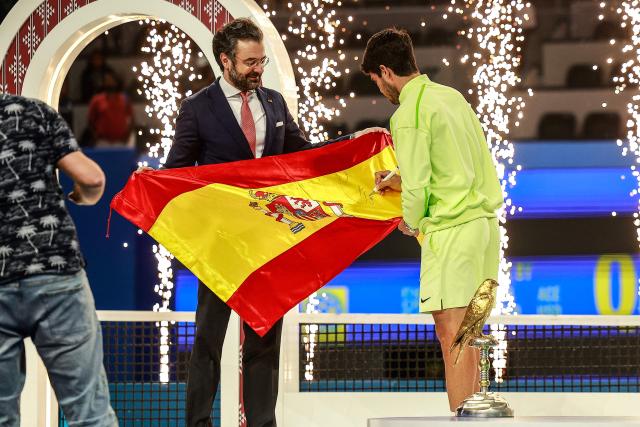 Spain's Carlos Alcaraz signs a Spanish flag as he celebrates after winning his men’s singles final match against France's Arthur Fils at the Qatar Open tennis tournament in Doha on February 21, 2026. (Photo by Karim JAAFAR / AFP)