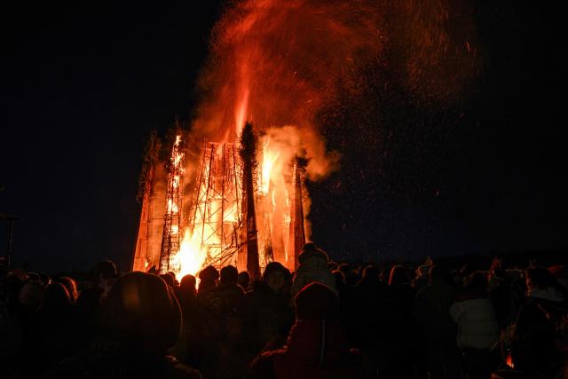 Spectators wearing customes watch the burning of the 'Burning Heart", a wooden structure created by Russian artist Nikolay Polissky, during celebrations of "Maslenitsa", the eastern Slavic Shrovetide in the village of Nikola-Lenivets, Kaluga region, some 220 km (140 miles) outside Moscow, on February 21, 2026. Shrovetide or Maslenitsa is an ancient farewell ceremony to winter, traditionally celebrated in Belarus, Russia and Ukraine and involves the burning of a large effigy. (Photo by HECTOR RETAMAL / AFP)