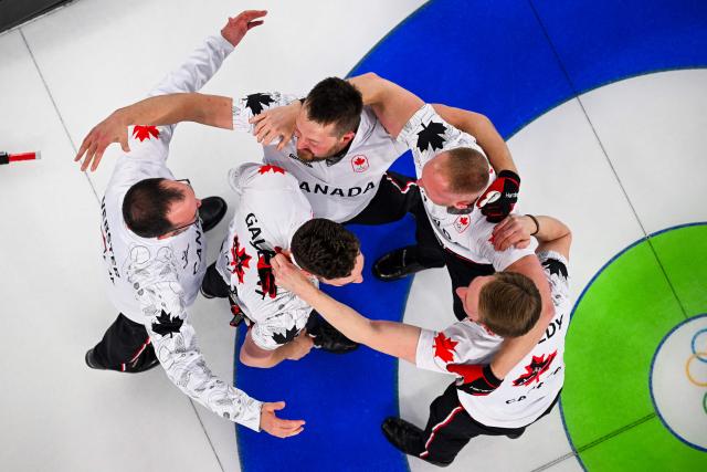 Team Canada celebrate becoming Olympic Champions as Britain's Hammy Mcmillan walks off after defeating team GB in the curling men's gold medal game between Great Britain and Canada during the Milano Cortina 2026 Winter Olympic Games at the Cortina Curling Olympic Stadium in Cortina d’Ampezzo on February 21, 2026. (Photo by Franзois-Xavier MARIT / AFP)