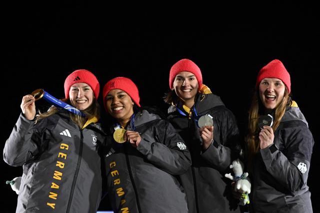 Gold medallists Germany's Laura Nolte and Germany's Deborah Levi (L) and silver medallists Germany's Lisa Buckwitz and Germany's Neele Schuten (R)  pose on the podium after the women's 2-woman heat 4 at Cortina Sliding Centre during the Milano Cortina 2026 Winter Olympic Games in Cortina d'Ampezzo on February 21, 2026. (Photo by Tiziana FABI / AFP)