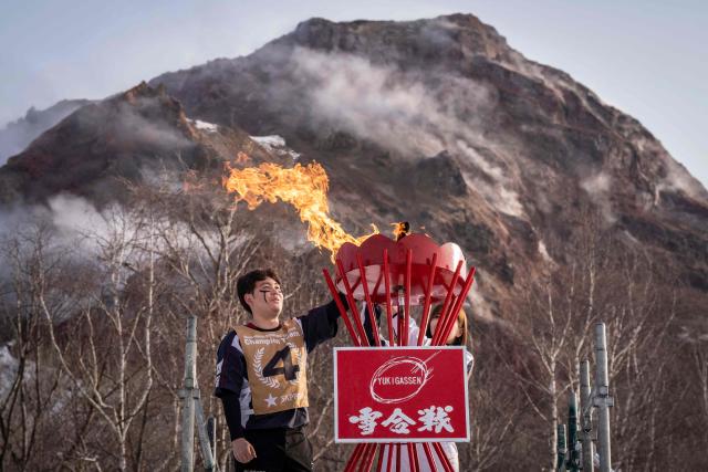 A player lights a cauldron for the Showa-shinzan International Yukigassen snowball fight competition in Sobetsu, Hokkaido prefecture on February 21, 2026. At the foot of an active volcano in northern Japan, shouts ring out, competitors size each other up and snowballs whistle through the air in a very serious game of "yukigassen" -- a sport with Olympic dreams. (Photo by Yuichi YAMAZAKI / AFP) / To go with 'JAPAN-SPORT-OLY, REPORTAGE' by Mathias CENA