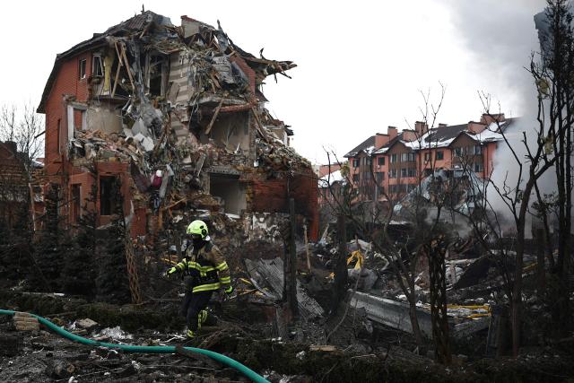 A Ukrainian rescuer walks among debris in front of a damaged house following an air attack in Sofiivska Borshchagivka, Kyiv region on February 22, 2026, amid the Russian invasion of Ukraine. Explosions rocked Ukraine's capital Kyiv with officials warning of a ballistic missile attack, just two days before the fourth anniversary of Russia's invasion. (Photo by Henry Nicholls / AFP)
