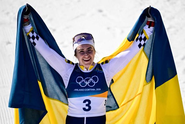 Sweden's Ebba Andersson celebrates with a flag of Sweden after crossing the finish line to win the women's cross country 50km mass start final event of the Milano Cortina 2026 Winter Olympic Games at Tesero Cross-Country Skiing Stadium in Lago di Tesero (Val di Fiemme), on February 22, 2026. (Photo by Tobias SCHWARZ / AFP)