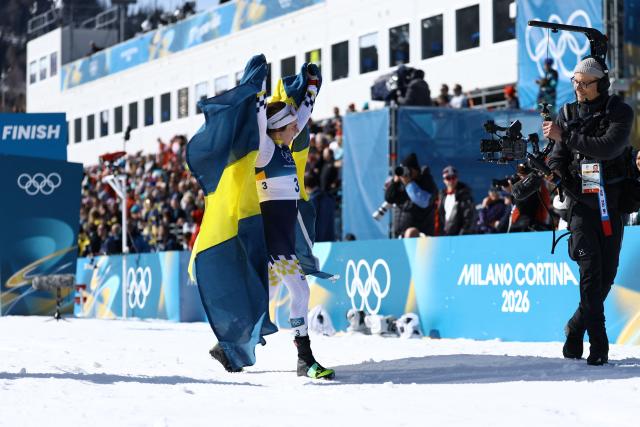 Sweden's Ebba Andersson celebrates with a flag of Sweden after crossing the finish line to win the women's cross country 50km mass start final event of the Milano Cortina 2026 Winter Olympic Games at Tesero Cross-Country Skiing Stadium in Lago di Tesero (Val di Fiemme), on February 22, 2026. (Photo by Anne-Christine POUJOULAT / AFP)