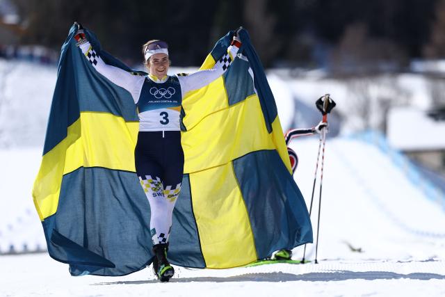 Sweden's Ebba Andersson celebrates with a flag of Sweden after crossing the finish line to win the women's cross country 50km mass start final event of the Milano Cortina 2026 Winter Olympic Games at Tesero Cross-Country Skiing Stadium in Lago di Tesero (Val di Fiemme), on February 22, 2026. (Photo by Anne-Christine POUJOULAT / AFP)