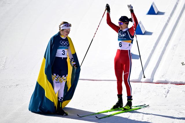 Sweden's Ebba Andersson (L) and Norway's Heidi Weng celebrate at the end of the women's cross country 50km mass start final event of the Milano Cortina 2026 Winter Olympic Games at Tesero Cross-Country Skiing Stadium in Lago di Tesero (Val di Fiemme), on February 22, 2026. (Photo by Tobias SCHWARZ / AFP)