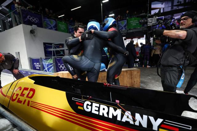Germany's Adam Ammour, Germany's Issam Ammour, Germany's Joshua Tasche and Germany's Alexander Schaller react after competing in the bobsleigh men's 4-man heat 4 at Cortina Sliding Centre during the Milano Cortina 2026 Winter Olympic Games in Cortina d'Ampezzo on February 22, 2026. (Photo by FRANCK FIFE / AFP)