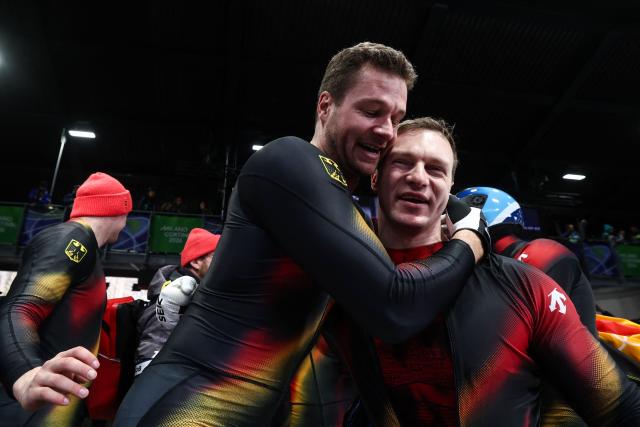 Gold medallist Germany's Johannes Lochner (L) congratulates silver medallist Germany's Francesco Friedrich (R) after competing with their team in the bobsleigh men's 4-man heat 4 at Cortina Sliding Centre during the Milano Cortina 2026 Winter Olympic Games in Cortina d'Ampezzo on February 22, 2026. (Photo by FRANCK FIFE / AFP)