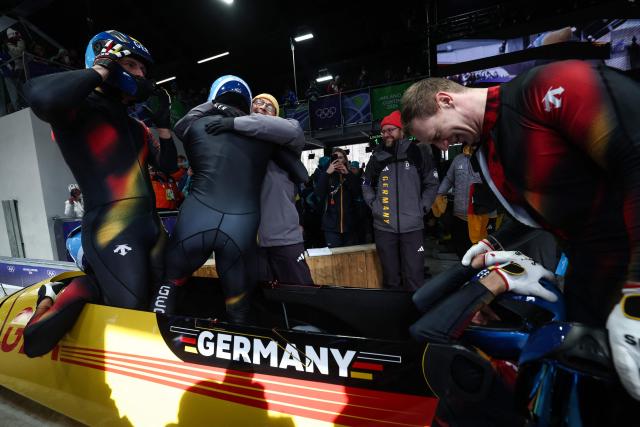Silver medallist Germany's Francesco Friedrich (R) congratulates the gold medallist team : Germany's Johannes Lochner, Germany's Thorsten Margis, Germany's Jorn Wenzel and Germany's Georg Fleischhauer after competing in the bobsleigh men's 4-man heat 4 at Cortina Sliding Centre during the Milano Cortina 2026 Winter Olympic Games in Cortina d'Ampezzo on February 22, 2026. (Photo by FRANCK FIFE / AFP)