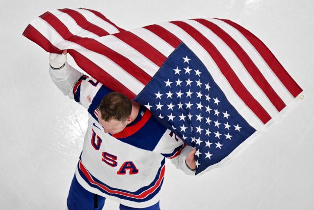 USA's #07 Brady Tkachuk waves the US flag after winning the men's gold medal ice hockey match between Canada and USA at the Milano Santagiulia Ice Hockey Arena during the Milano Cortina 2026 Winter Olympic Games in Milan, on February 22, 2026. (Photo by Antonin THUILLIER / AFP)