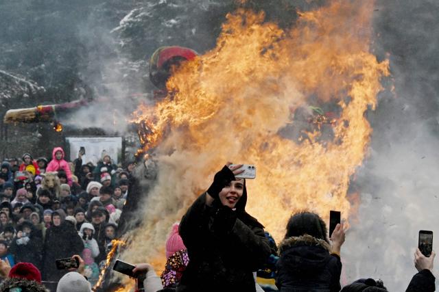 A woman poses for a selfie photo in front of a burning straw-wood-and-cloth effigy representing Mother Winter during Maslenitsa (Shrovetide), a traditional Slavic farewell ceremony to winter, in Pavlovsk, Leningrad region on February 22, 2026. Shrovetide precedes the beginning of Lent, with each day of the week holding its own meaning. Shrove Sunday, also known as the Sunday of Forgiveness, is a day for asking forgiveness for the harm caused to other people intentionally or unintentionally. (Photo by Olga MALTSEVA / AFP)