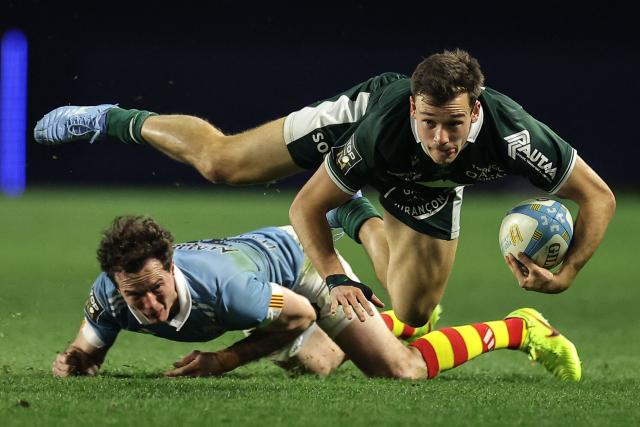 Pau's French full back Clement Mondinat (TOP) is tackled during the French Top 14 rugby union match between USA Perpignan and Section Paloise Bearn Pyrenees (Pau) at the Aime-Giral stadium in Perpignan, south-western France on February 22, 2026. (Photo by Valentine CHAPUIS / AFP)