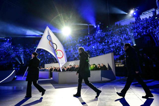 Milan mayor Giuseppe Sala (C) and Cortina d'Ampezzo mayor Gianluca Lorenzi (R) walk behind the Olympic flag during the flag handover ceremony at the closing ceremony of the Milano Cortina 2026 Winter Olympic Games at the Verona Arena in Verona, northern Italy, on February 22, 2026. (Photo by Stefano RELLANDINI / AFP)
