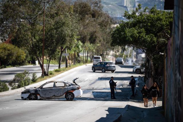 A burned taxi, allegedly set on fire by organized crime groups in response to an operation in Jalisco to arrest Nemesio Oseguera, leader of the violent Jalisco New Generation Cartel, is seen on International Avenue on the Mexican side of the US-Mexico border in Tijuana, in Baja California State, Mexico, February 22, 2026. Mexico confirmed on February 22 that soldiers killed a powerful drug cartel leader who was one of the most wanted men here and in the United States. Nemesio Oseguera, the 59-year-old leader of the violent Jalisco New Generation Cartel, was wounded in a clash with soldiers in the town of Tapalpa and died while being flown to Mexico City, the army said in a statement. (Photo by Guillermo Arias / AFP)