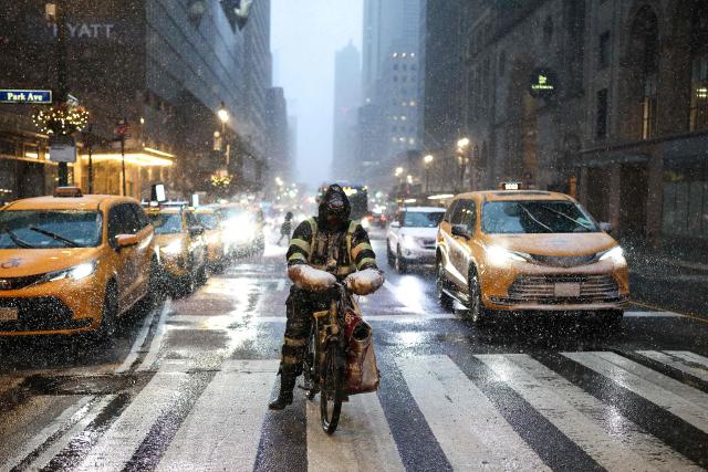 A man delivering food by bike rides along 42nd Street in the Manhattan borough of New York City on February 22, 2026. A fast-developing storm is threatening to pummel the US East Coast with a foot (30cm) or more of snow beginning Sunday, bringing Mother Nature's wrath to a region that only just dug out from a previous winter wallop. Meteorologists issued blizzard warnings for New York and parts of at least six states, warning Saturday that heavy snow and gale-force winds are forecast to slam all major cities along the densely populated Interstate 95 northeast corridor, including Philadelphia, Boston and even Washington further south. (Photo by CHARLY TRIBALLEAU / AFP)