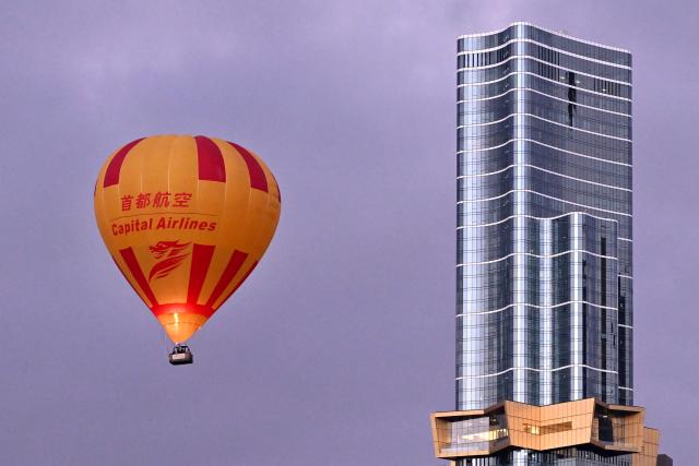 A hot-air balloon carrying tourists passes by the Melbourne central business district skyline during an early morning flight on February 23, 2026. (Photo by William WEST / AFP)