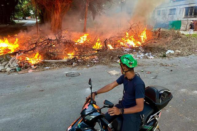 A motorcyclist watches the flames from a fire at an open-air garbage dumping site in a neighborhood of Havana, on February 22, 2026.  (Photo by Yamil LAGE / AFP)
