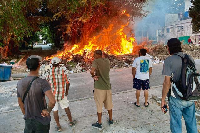 Residents watch the flames from a fire at an open-air garbage dumping site in a neighborhood of Havana, on February 22, 2026.  (Photo by Yamil LAGE / AFP)