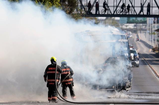 Firefighters extinguish a burning bus set on fire by organised crime groups in response to an operation in Jalisco to arrest a high-priority security target, at one of the main avenues in Zapopan, state of Jalisco, Mexico, on February 22, 2026. Armed civilians blocked several roads in the state of Jalisco, in western Mexico, following an operation by federal forces in the town of Tapalpa, local authorities reported. Jalisco, which will host four matches of the upcoming 2026 World Cup, is home to the powerful Jalisco New Generation Cartel (CJNG), and has been rocked by several episodes of violence in recent years. (Photo by Ulises Ruiz / AFP)