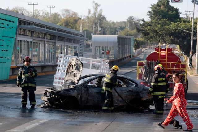 Firefighters extinguish a burning vehicle set on fire by organised crime groups in response to an operation in Jalisco to arrest a high-priority security target, at one of the main avenues in Zapopan, state of Jalisco, Mexico, on February 22, 2026. Armed civilians blocked several roads in the state of Jalisco, in western Mexico, following an operation by federal forces in the town of Tapalpa, local authorities reported. Jalisco, which will host four matches of the upcoming 2026 World Cup, is home to the powerful Jalisco New Generation Cartel (CJNG), and has been rocked by several episodes of violence in recent years. (Photo by Ulises Ruiz / AFP)