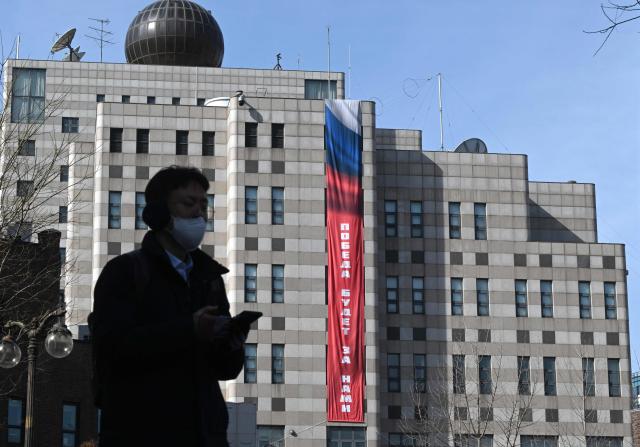 A man walks in front of the Russian embassy in Seoul on February 23, 2026, as a banner reading "Victory will be ours" is displayed on the exterior wall of the embassy. South Korea has protested to Russia after its embassy in Seoul unfurled a giant banner declaring "Victory will be ours", an apparent reference to the anniversary of the Ukraine war. (Photo by Jung Yeon-je / AFP)