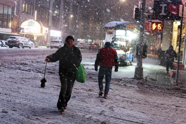 People walk along Manhattan's 8th Avenue during a snowfall in New York City, on February 22, 2026. A fast-developing storm is threatening to pummel the US East Coast with a foot (30cm) or more of snow beginning Sunday, bringing Mother Nature's wrath to a region that only just dug out from a previous winter wallop. Meteorologists issued blizzard warnings for New York and parts of at least six states, warning Saturday that heavy snow and gale-force winds are forecast to slam all major cities along the densely populated Interstate 95 northeast corridor, including Philadelphia, Boston and even Washington further south. (Photo by CHARLY TRIBALLEAU / AFP)