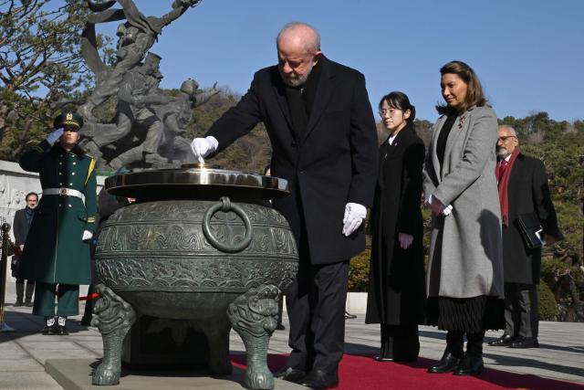 Brazil's President Luiz Inacio Lula da Silva (C) burns incense as his wife Rosangela da Silva (R) looks on at the National Cemetery in Seoul on February 23, 2026, during his state visit to South Korea. (Photo by Jung Yeon-je / AFP)