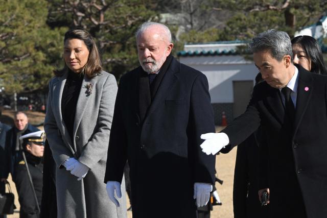 Brazil's President Luiz Inacio Lula da Silva (C) and his wife Rosangela da Silva (L) visit the National Cemetery in Seoul on February 23, 2026, during his state visit to South Korea. (Photo by Jung Yeon-je / AFP)