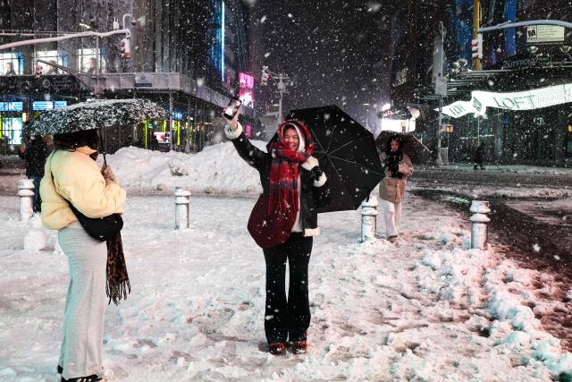 A woman uses her smartphone while enjoying a snowfall around Manhattan's Times Square in New York City, on February 22, 2026. A fast-developing storm is threatening to pummel the US East Coast with a foot (30cm) or more of snow beginning Sunday, bringing Mother Nature's wrath to a region that only just dug out from a previous winter wallop. Meteorologists issued blizzard warnings for New York and parts of at least six states, warning Saturday that heavy snow and gale-force winds are forecast to slam all major cities along the densely populated Interstate 95 northeast corridor, including Philadelphia, Boston and even Washington further south. (Photo by CHARLY TRIBALLEAU / AFP)