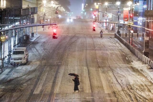 A woman crosses a street near Manhattan's Grand Central during a snowfall in New York City, on February 22, 2026. A fast-developing storm is threatening to pummel the US East Coast with a foot (30cm) or more of snow beginning Sunday, bringing Mother Nature's wrath to a region that only just dug out from a previous winter wallop. Meteorologists issued blizzard warnings for New York and parts of at least six states, warning Saturday that heavy snow and gale-force winds are forecast to slam all major cities along the densely populated Interstate 95 northeast corridor, including Philadelphia, Boston and even Washington further south. (Photo by CHARLY TRIBALLEAU / AFP)