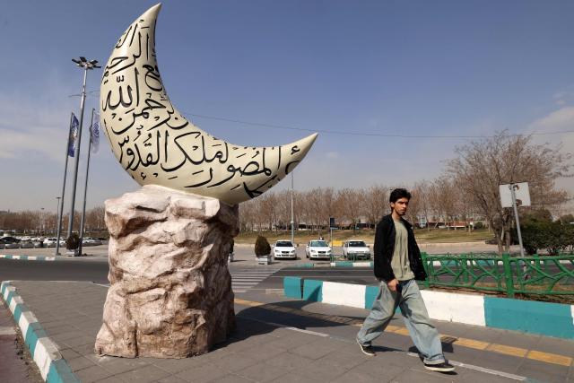 A man walks past a sculpture depicting a crescent moon covered with inscriptions of the Islamic names of God, set up for the Holy month of Ramadan, in Tehran on February 23, 2026. (Photo by ATTA KENARE / AFP)