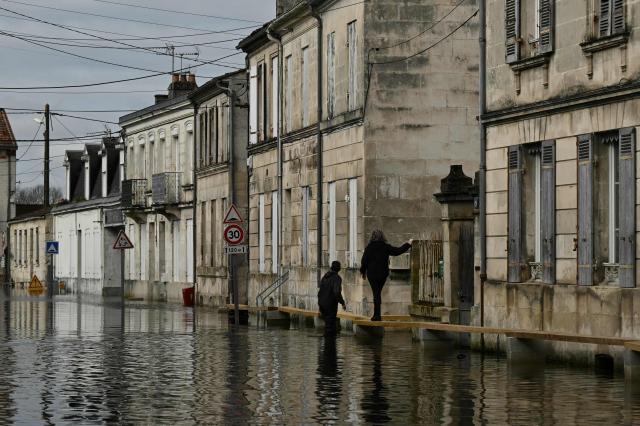 Residents walk on wooden planks above the water on a flooded street following severe flooding from storm Nils in Saintes, south-western France, on February 23, 2026. (Photo by Philippe LOPEZ / AFP)