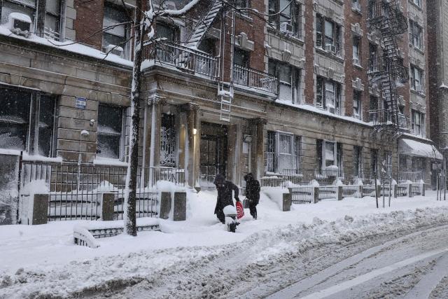 People walk in the falling snow during a winter storm in the Manhattan borough of New York City on February 23, 2026. New York ordered drivers off the road and shut down schools on Monday, while residents hunkered down for a massive snowstorm hitting the United States northeast. The National Weather Service (NWS) said in a post on X that "heavy snow is still falling" at 5:28 am local time (1028 GMT) on Monday adding that a the total snowfall stands at 14.9 inches. (Photo by CHARLY TRIBALLEAU / AFP)